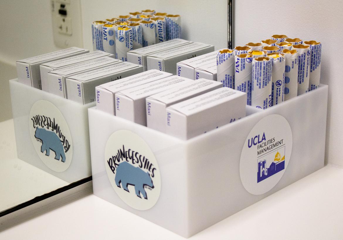 Boxes of menstrual hygiene products on a desk, with UCLA branding