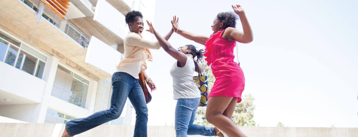 Three Black women jumping to high five eachother