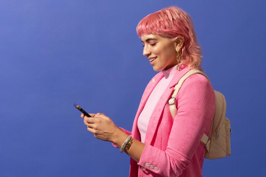 A person with pink hair in a pink blazer holding up their phone to text