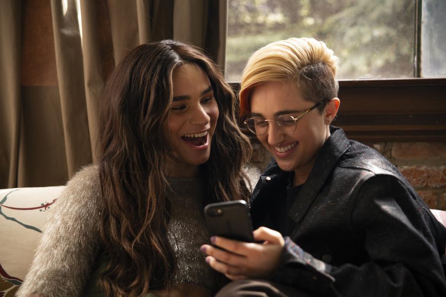 A transfeminine non-binary person and transmasculine gender-nonconforming person looking at a photo