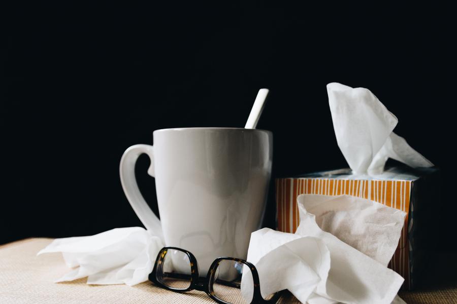 On a white counter with a black background, a coffee cup with stirrer, glasses, tissue paper scrunched, and striped tissue paper box